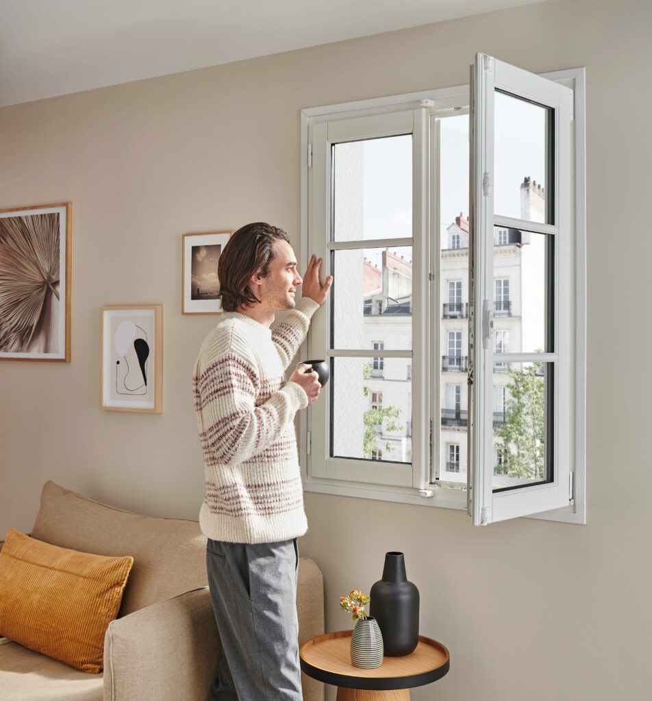 Homme devant une fenêtre ouverte dans son appartement